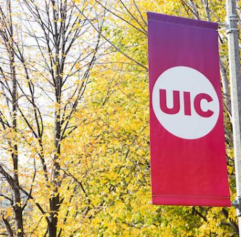 A UIC banner on a pole with yellowing leafed-trees in the background. 